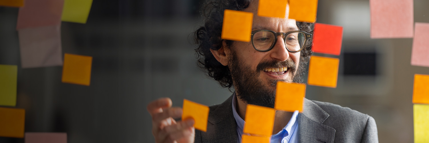 adult man smiling and while adding sticky notes to a glass wall